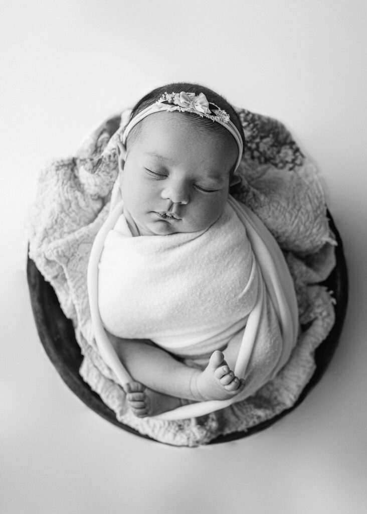 baby girl wrapped in a bowl prop, black and white digital image, baby girl sleeping during her newborn photography session, quilt piece used for layer under newborn baby