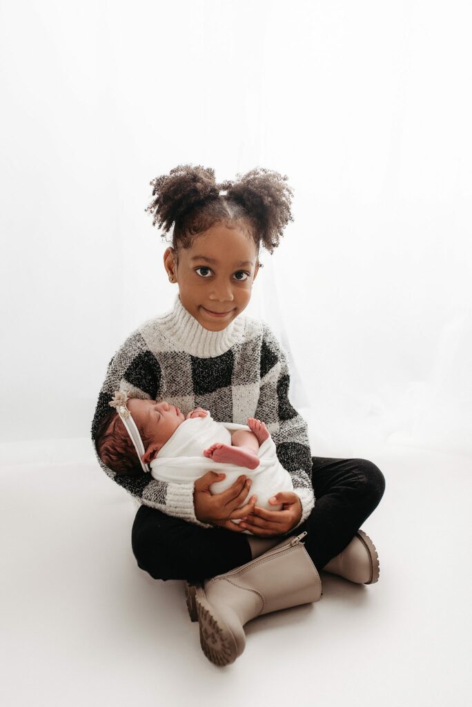 family photoshoot in studio on white backdrop, toddler posed with new baby sister, family photographer in atlanta, atlanta newborn photography studio