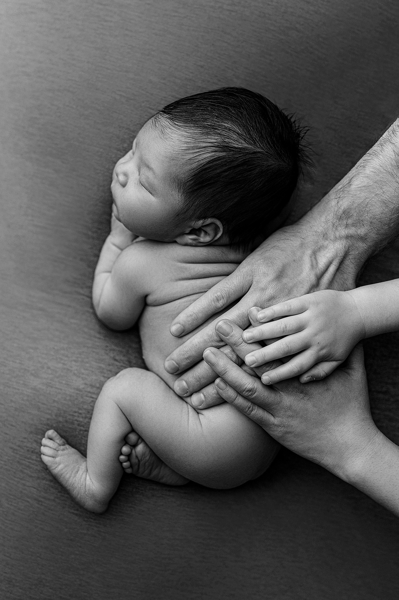 baby boy in black and white with his parents hands on him to show how little he is, newborn photoshoot near me